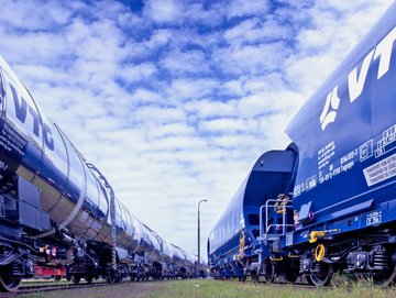 Silvery VTG chemical tank wagon next to blue VTG standard freight wagon under blue sky