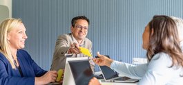 Company Four people in a meeting; a man hands a yellow note to a woman across the table. Everyone appears friendly and engaged.