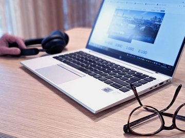 Smiling woman with long brown hair in an office sits in front of her laptop.